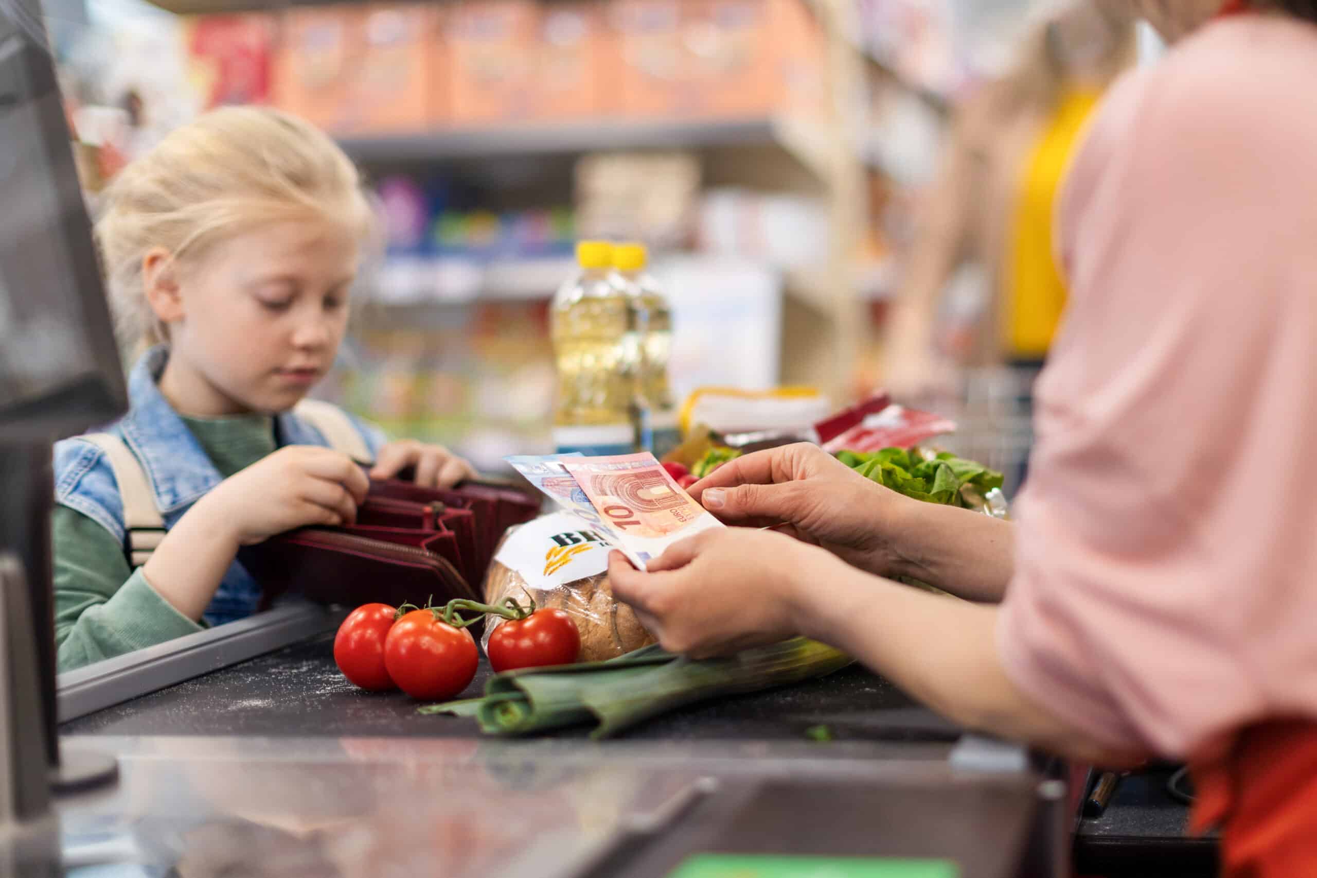 Nahaufnahme eines kleinen blonden Mädchens, das im Supermarkt für den Lebensmitteleinkauf bezahlt.